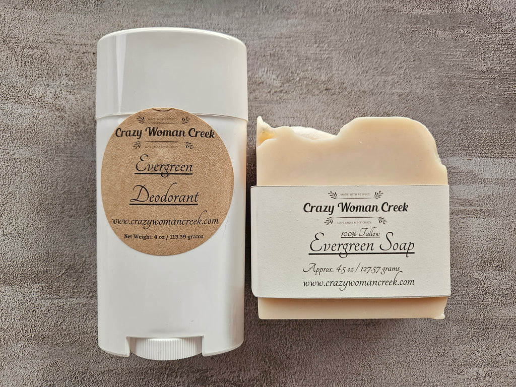 A white plastic deodorant stick and a bar of soap from Crazy Woman Creek, both labeled 'Evergreen' and  arranged on a textured gray background.