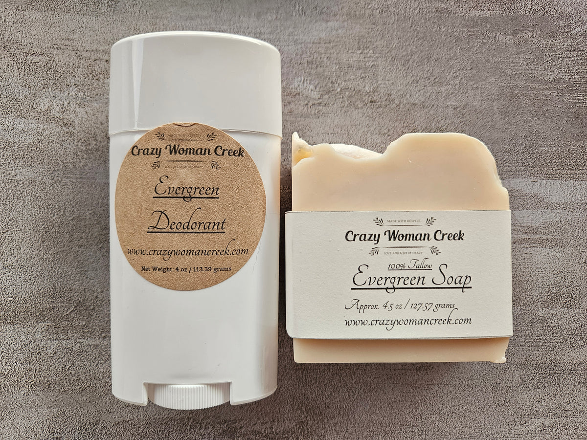 A white plastic deodorant stick and a bar of soap from Crazy Woman Creek, both labeled 'Evergreen' and  arranged on a textured gray background.