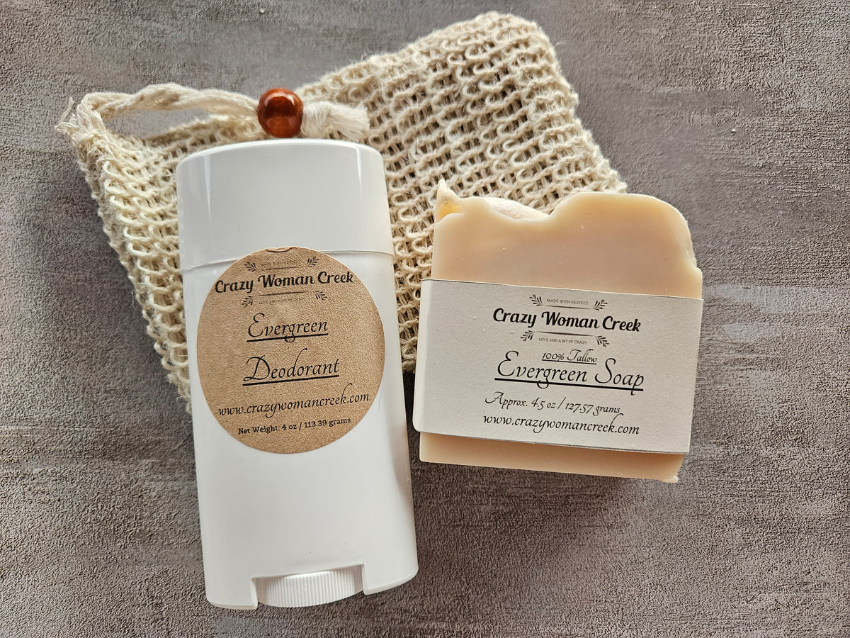 A white cylindrical deodorant bottle and a bar of handmade soap with a paper band label, both made by Crazy Woman Creek, arranged on a beige crochet soap bag. 